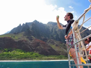 Man taking pictures of the Napali coast from the railing of a boat.