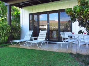 Picture of lanai with table seating for four on right and two lounge chairs on the left. Behind is four large glass panels with center sliding doors to enter the condo.