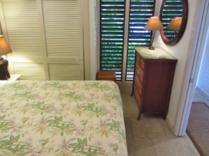 Picture of the bedroom showing part of the bed, the nightstand's lamp, the closet, the dresser, and the louvered full length windows.